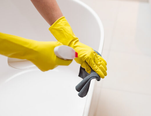 Hands with yellow rubber gloves holding detergent spray bottle and cleaning bath in bathroom. Spring cleaning